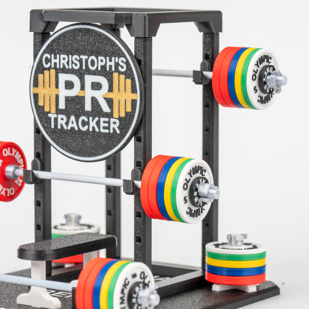 Weightlifting rack with colorful Olympic plates and a branded 'PR Tracker' sign.